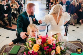 A child blows out a candle during a wedding celebration at City Hall Dublin. The bride and groom are distracted and unaware of the child’s action.